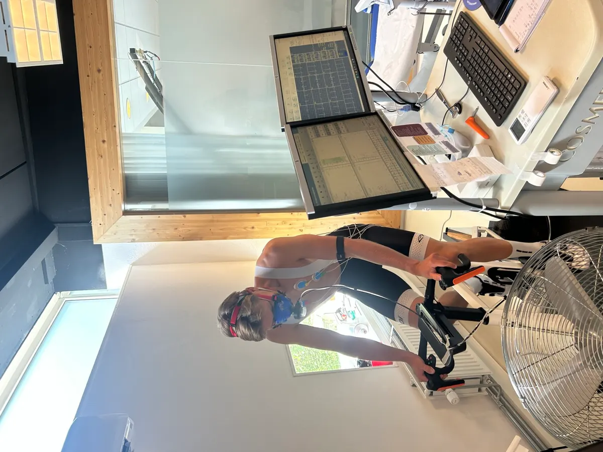 Daniël Beerdsen staand op de pedalen tijdens een inspanningstest, met ademmasker en ECG-elektrodes